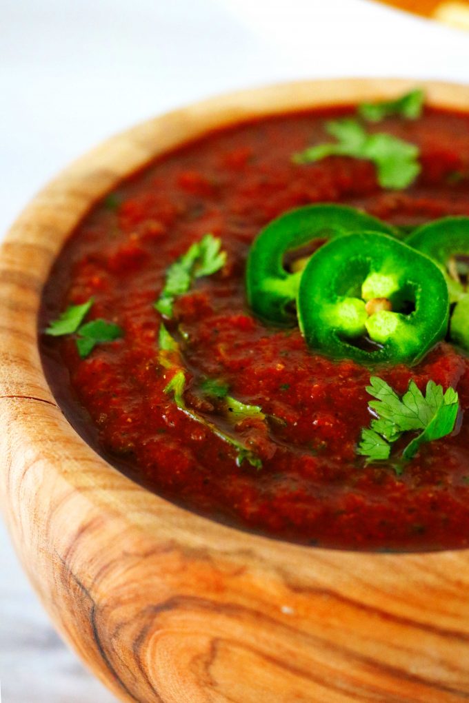 A small wood bowl with Mexican salsa inside and a jalapeno and cilantro garnish on top.