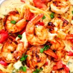 An overhead shot of Cajun Shrimp Pasta in a pan garnished with sliced green onions and diced tomatoes.