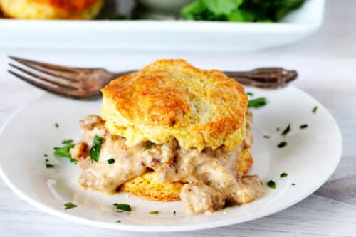 A biscuit with sawmill gravy on a white plate with a fork behind it.