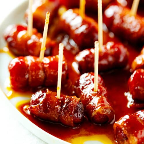 Bacon Wrapped Smokies on a plate with toothpicks sticking out of them.