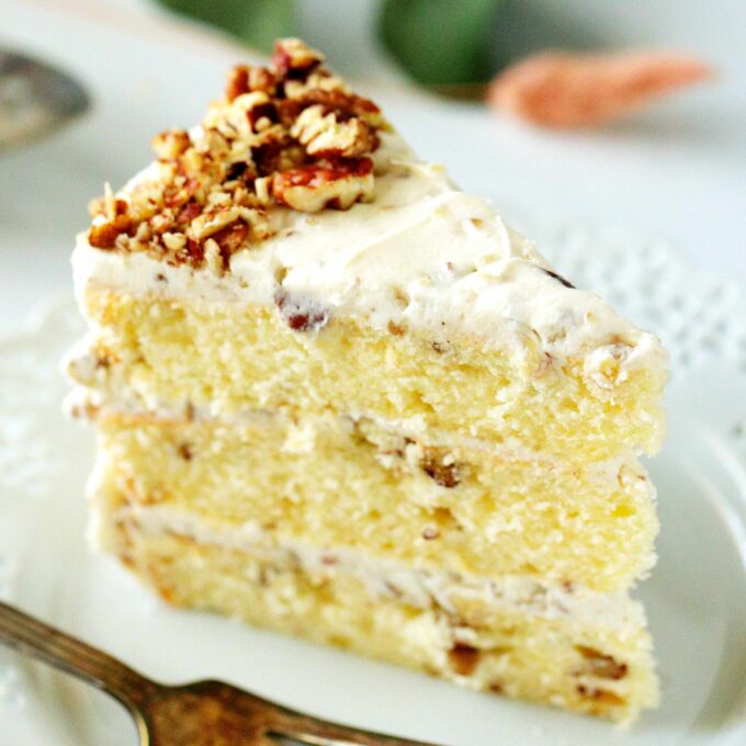 A slice of three layer Butter Pecan Cake on a white plate with a fork next to it.