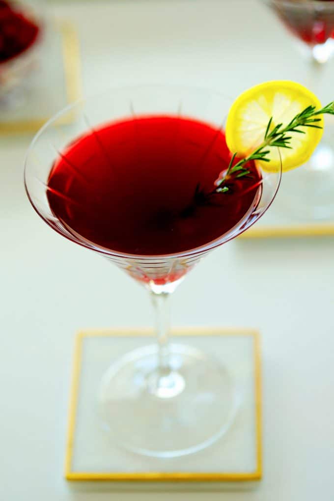 A trio of pomegranate martinis with a lemon wheel wedge and rosemary garnish.