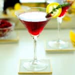 A pomegranate martini with a lemon wheel wedge and rosemary garnish.
