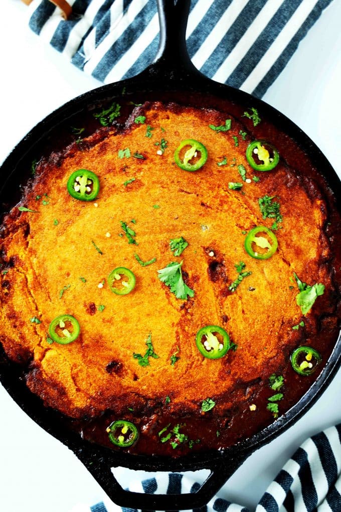 An overhead shot of of tamale pie in a cast iron skillet with jalapenos and cilantro on top.