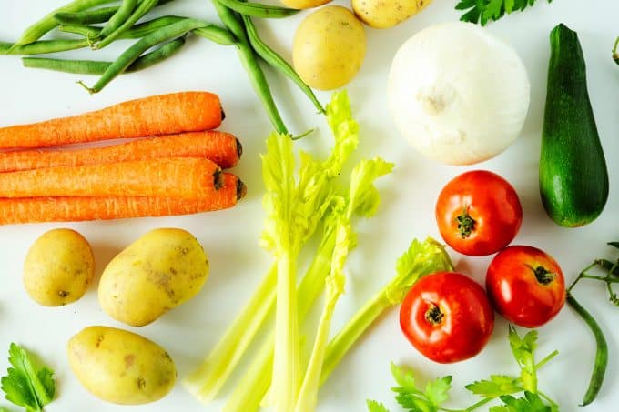 Carrots, potatoes, green beans, celery, tomatoes, onions and zucchini on a white background.