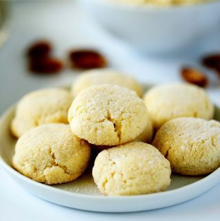 A bundle of amaretti cookies on a white plate with almonds around it.