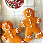 Two gingerbread cookies on a cooling rack with a bowl of sprinkles off to the side.