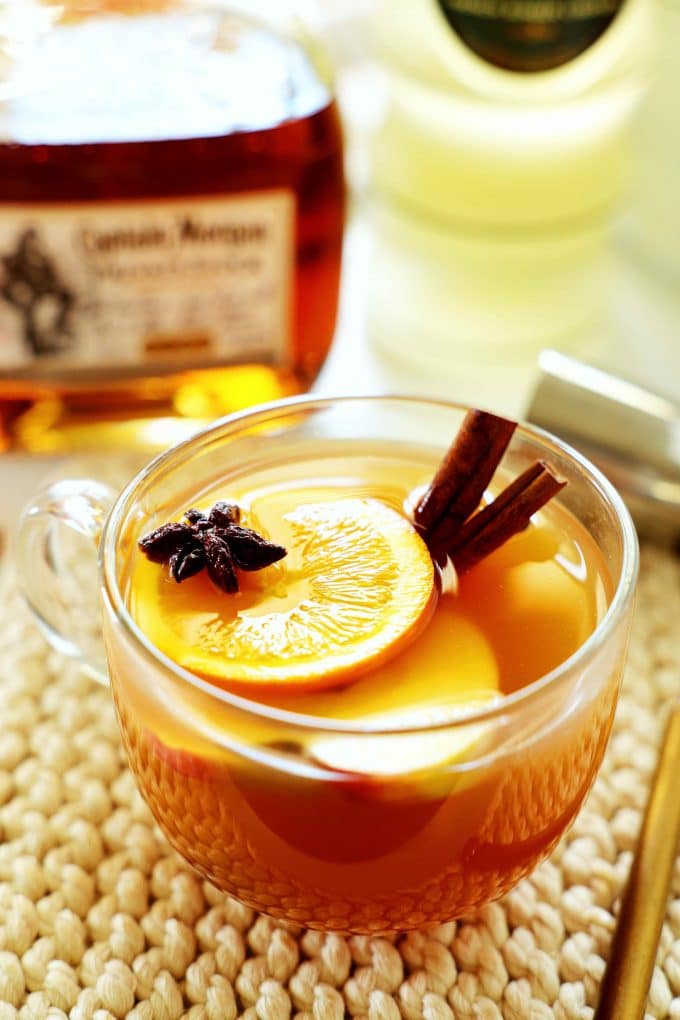 A mug of hot spiked apple cider with rum and liqueur in the background.