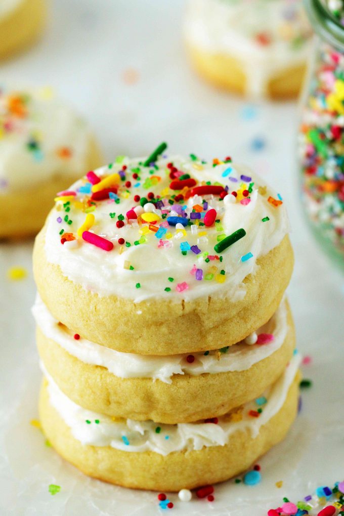 A stack of iced sugar cookies with sprinkles off to the side.