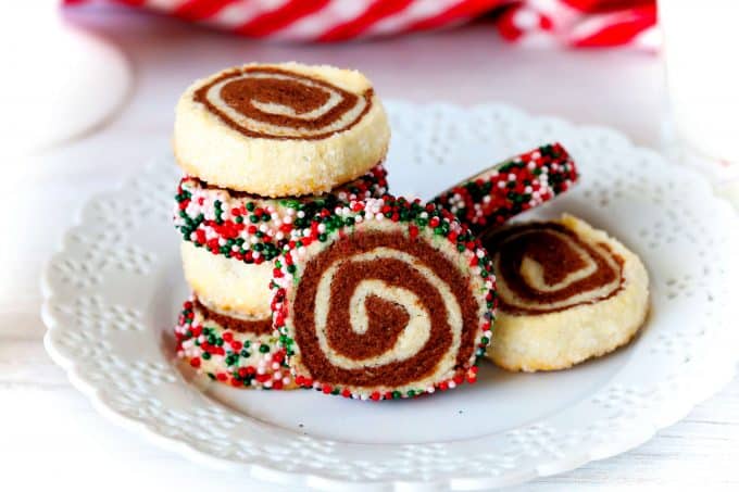 Christmas colored Pinwheel Cookies on white plate with a red plaid towel behind it.