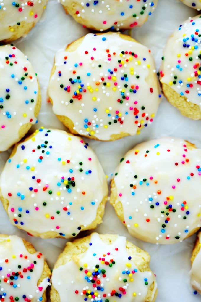 An overhead shot of Sour Cream Cookies with a white glaze and sprinkles spread out on a white surface.