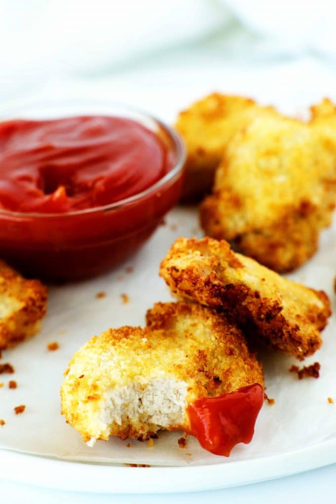 An air fryer chicken nugget with a bite taken out of it and a bowl of ketchup behind it.