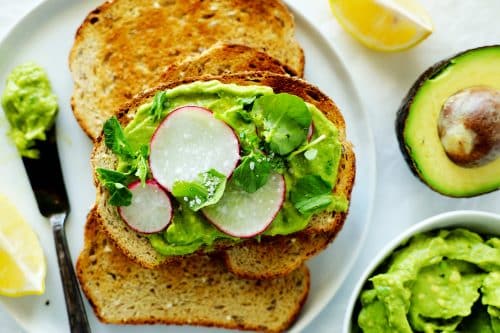 Toast with avocado spread, radishes, and watercress on a plate with other pieces of toast.
