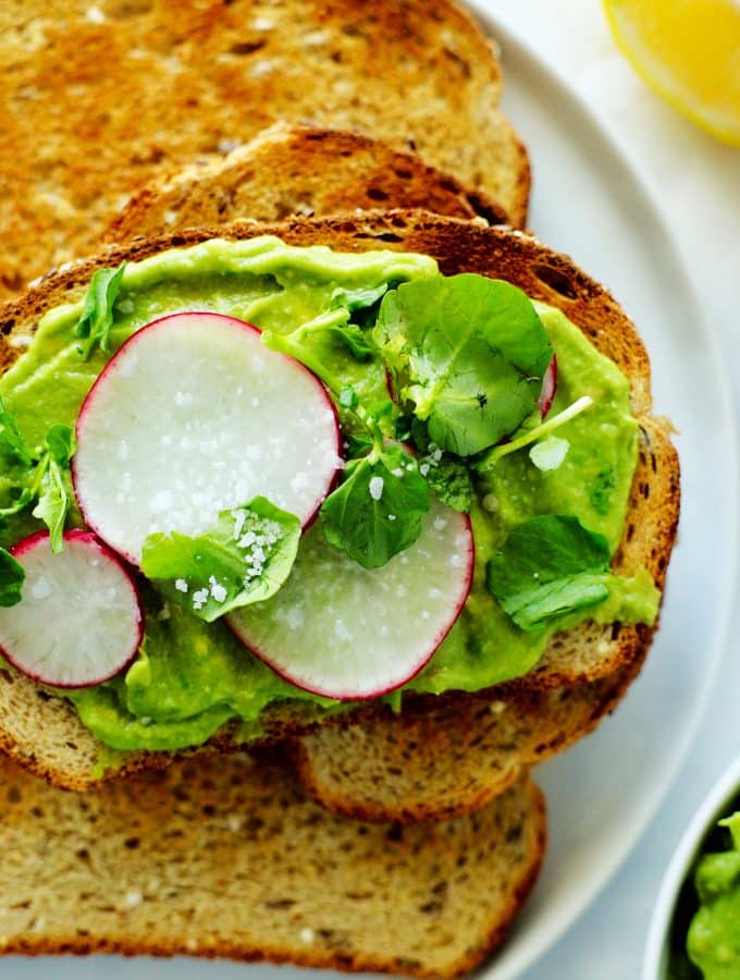 Toast with avocado spread, radishes, and watercress on a plate with other pieces of toast.