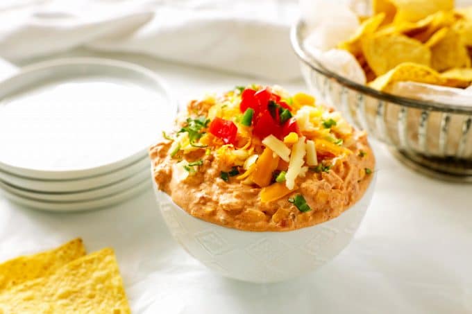 A bowl of cream cheese dip with taco toppings on top and tortilla chips off to the side. 