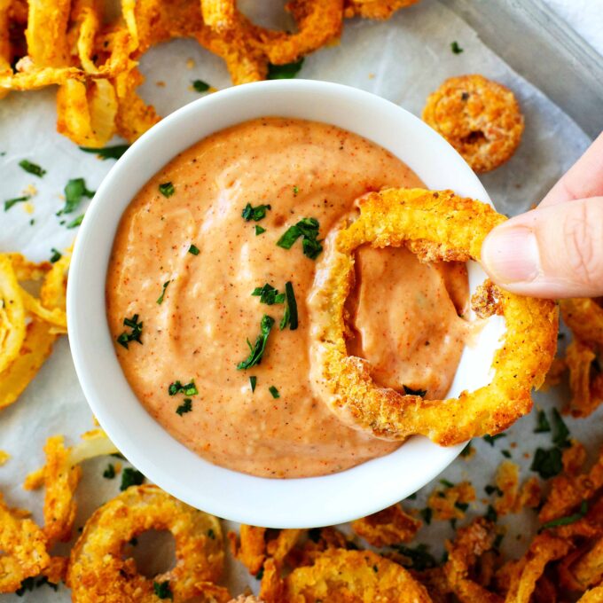 An overhead shot of an onion ring being dipped into comeback sauce.
