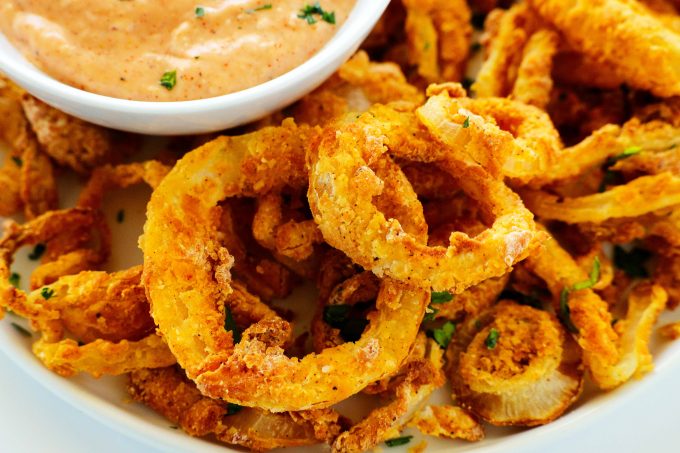 A close up shot of Air Fryer Onion Rings on a white plate with Comeback Sauce off to the side and a garnish of parsley. 