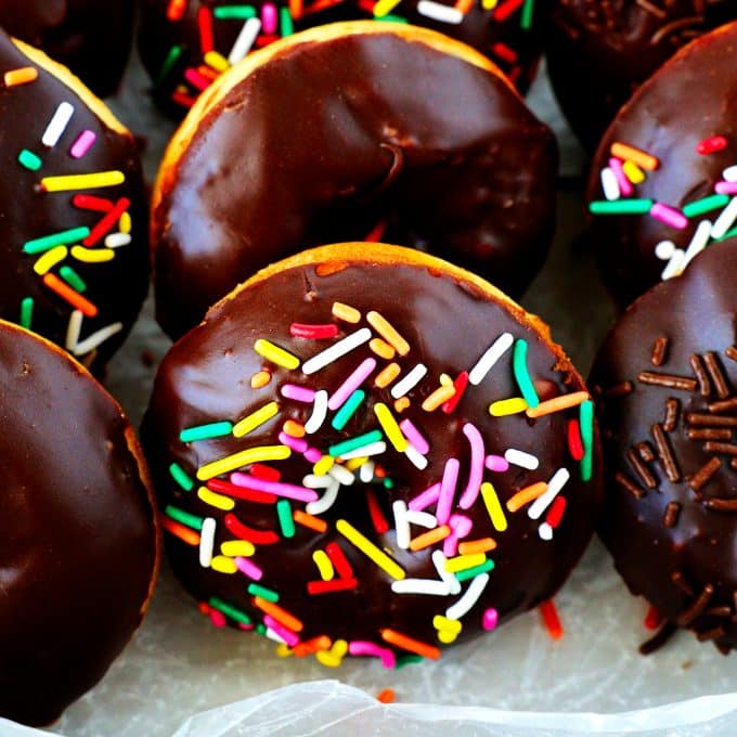 A close-up shot of chocolate glazed donuts with rainbow sprinkles in a box.