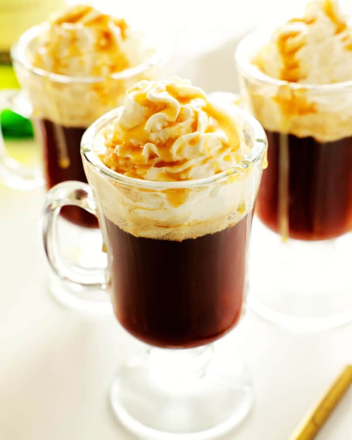 Three irish coffees topped with whipped cream and caramel.