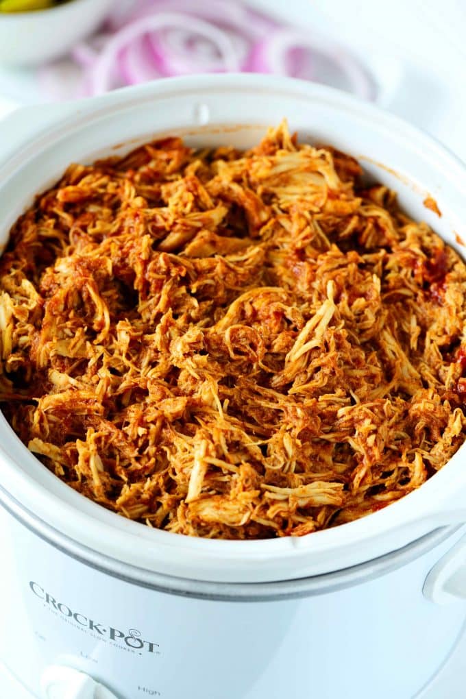 An overhead shot of slow cooker pulled chicken with onions in the background.
