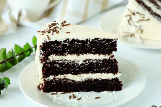 A slice of chocolate coffee cake with buttercream frosting on a white plate. 