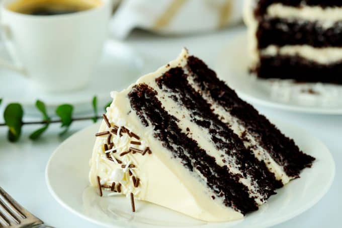 A slice of chocolate coffee cake with buttercream frosting on its side on a white plate. 
