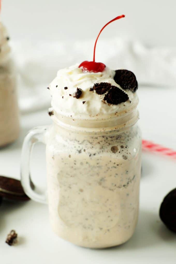 An oreo shake with whipped cream and a cherry on top. Oreos and a red straw are in the background.