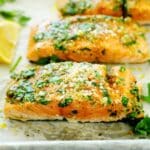 Individual fillets of Lemon Garlic Salmon laid out on a baking sheet with a lemon wedge off to the side.