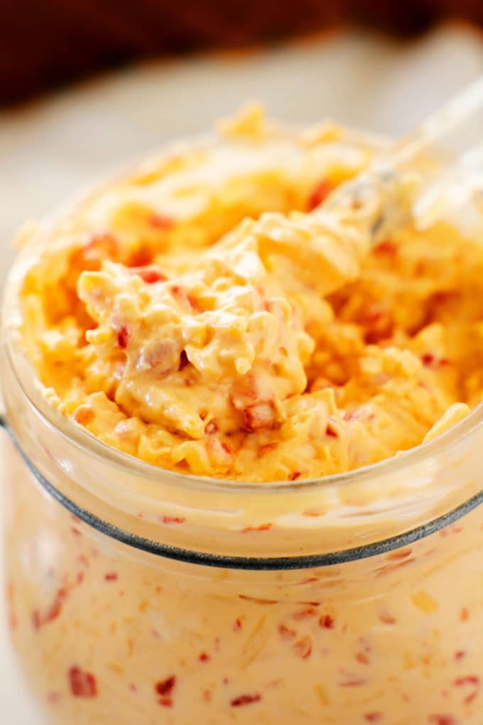 A close up shot of pimento cheese with a spreader scooping up out of it.