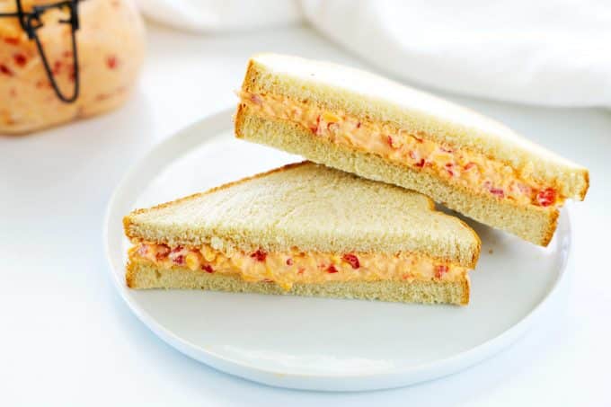 A pimento cheese sandwich sliced on the diagonal on a white plate.