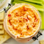 An overhead shot of pimento cheese in a jar on a plate with celery and crackers.