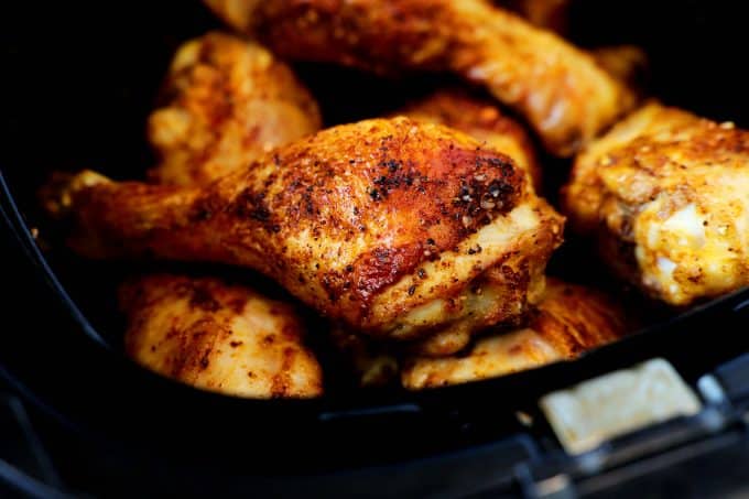 Cooked chicken legs stacked in the basket of an air fryer.