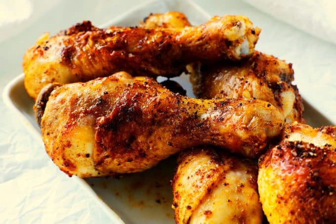 An overhead shot of air fryer chicken legs stacked on a white platter.