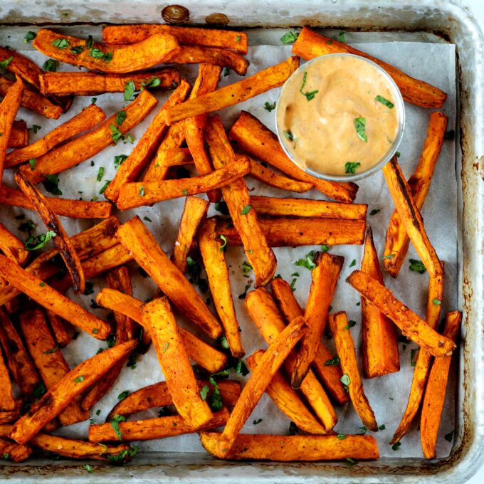 A close up, overhead shot of air fryer sweet potato fries on a baking sheet with fry sauce off to the sides. 