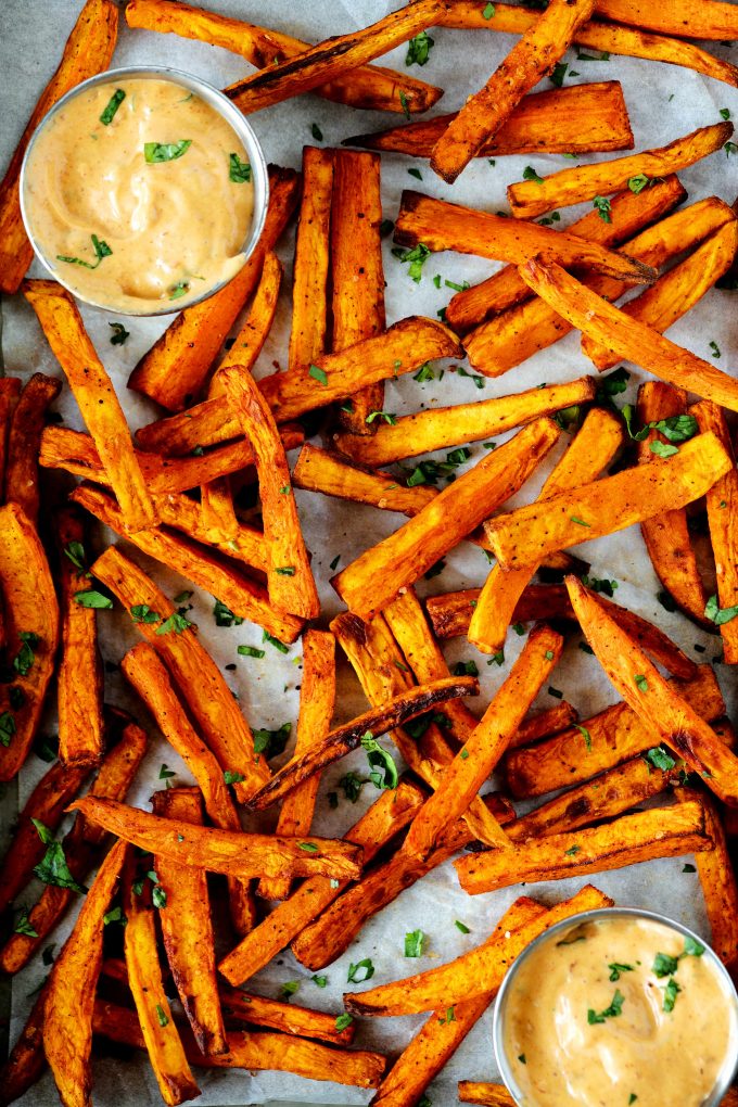 An overhead shot of air fryer sweet potato fries on a baking sheet with fry sauce off to the sides. 