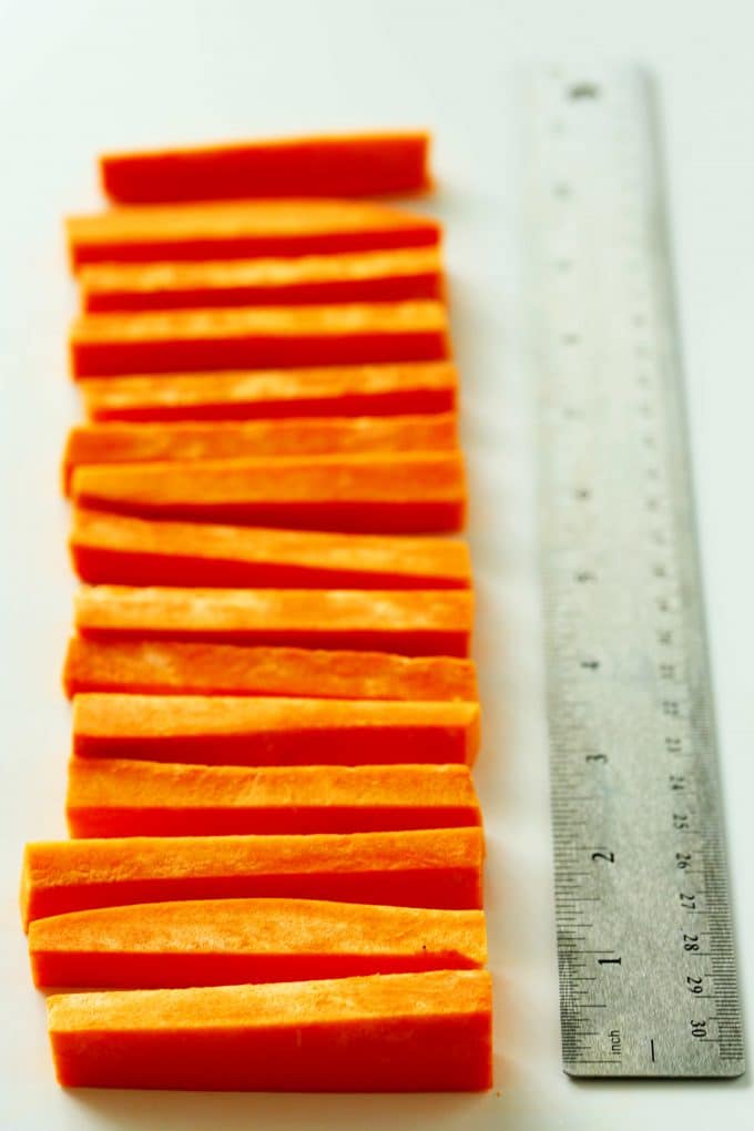 Raw, cut sweet potato fries in a line next to a ruler.
