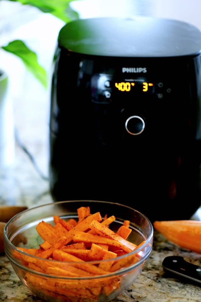 Sweet potatoes in a bowl with an air fryer in the background.
