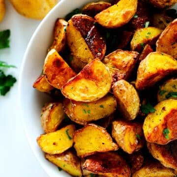 Roasted Baby potatoes in a white bowl with fresh potatoes off to the side.