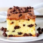 A slice of chocolate chip cake on a white plate with chocolate chips surrounding it.