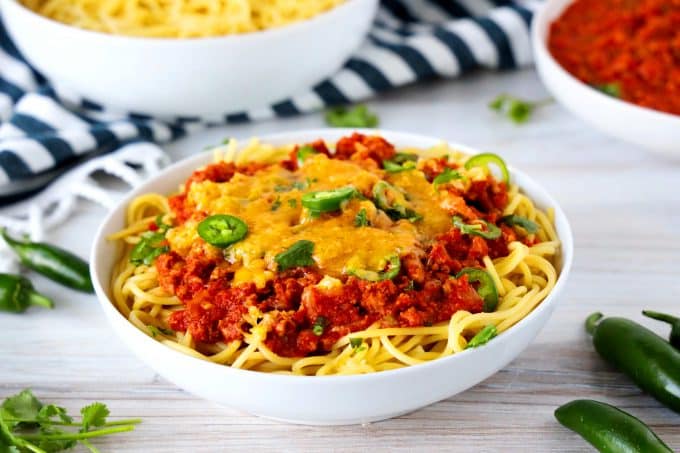 Mexican spaghetti in a white bowl with cheese and jalapenos on top and spaghetti noodles off to the side.