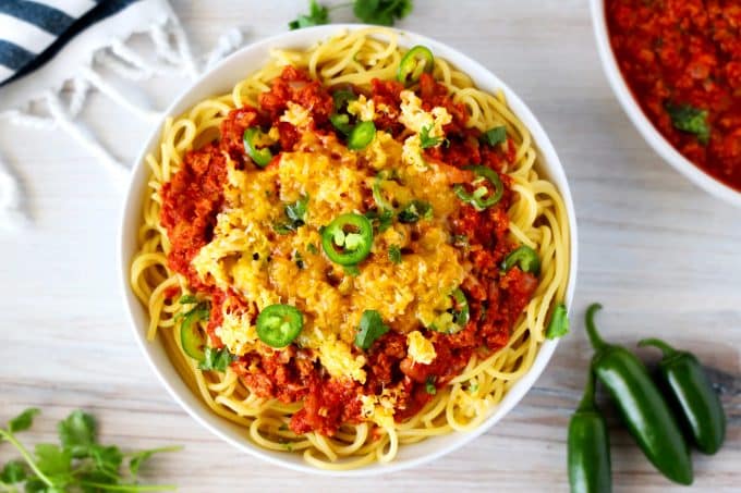 And overhead shot of Mexican spaghetti in a white bowl with cheese and jalapenos on top and sauce off to the side.
