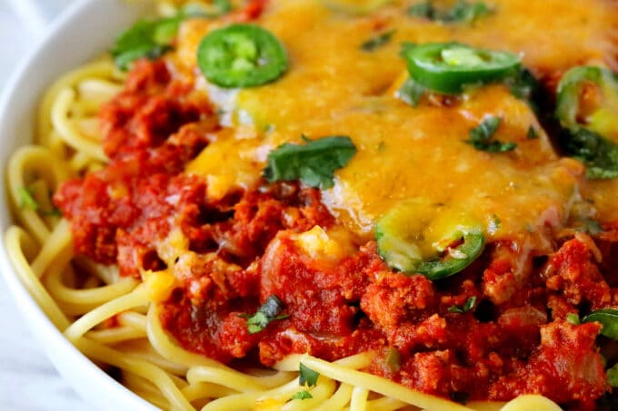 A close up shot of Mexican spaghetti in a white bowl with cheese and jalapenos on top.
