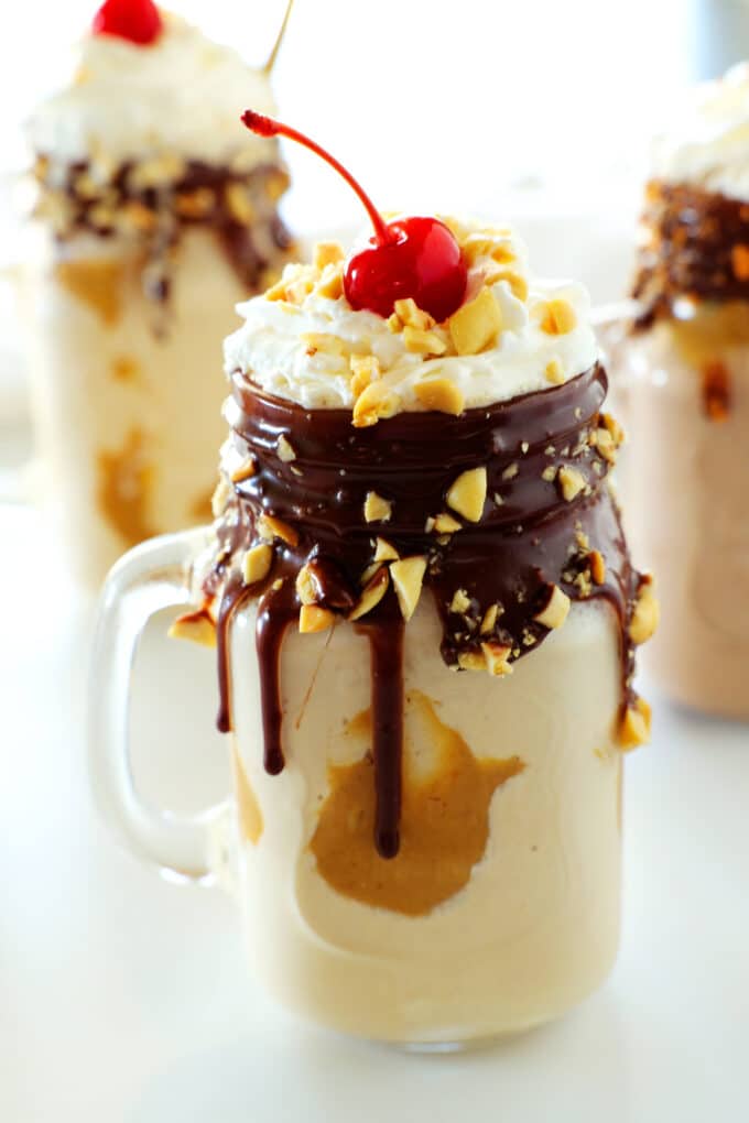 Peanut butter milkshake with a whipped cream topping, chopped peanuts, and a cherry on top.