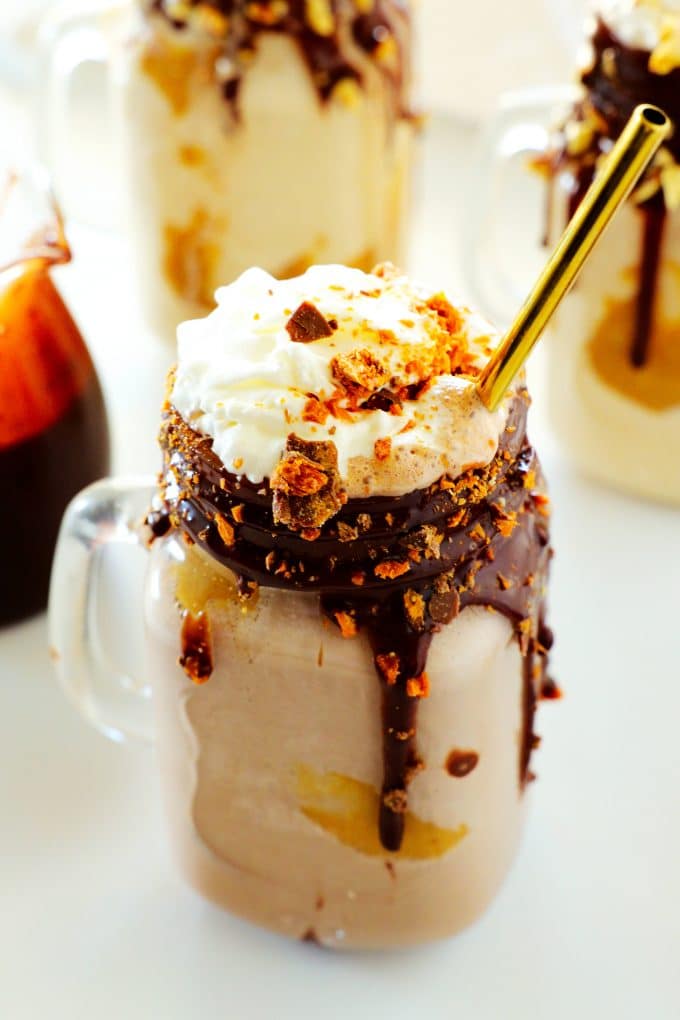 A close up up a peanut butter milkshake with a whipped cream topping and crushed butterfinger candy on top.