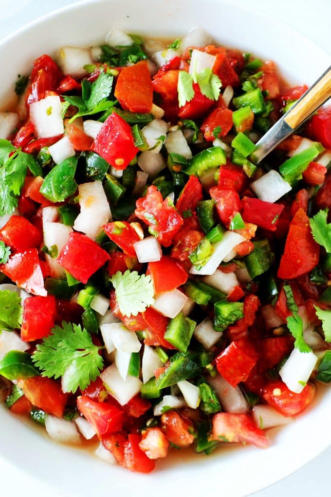 A close up, overhead shot of Pico de gallo in a white bowl with a spoon in it.