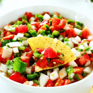 Pico de gallo in a white bowl with a chip dipped in it.