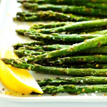 Air fryer asparagus on a white plate with a lemon wedge off to the side.
