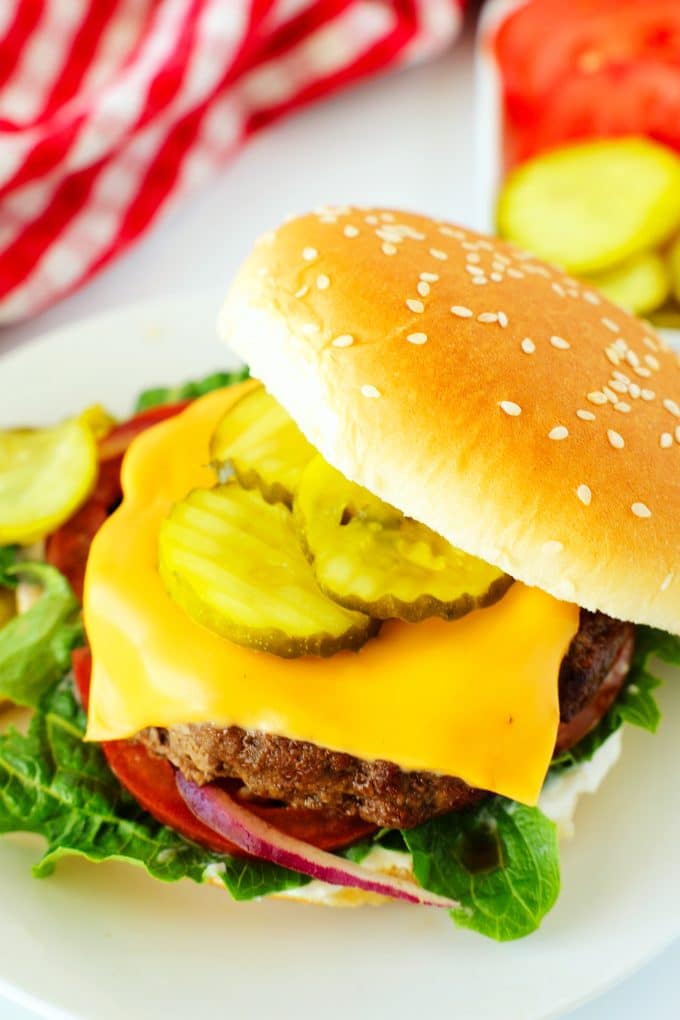 An air fryer burger topped with cheese and vegetables with the bun half on top of it and slightly opened.