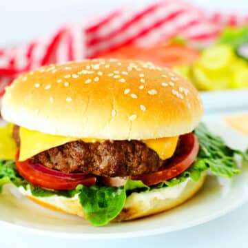 Air fryer burgers with cheese and vegetables on a white plate with a checkered red towel in the background.