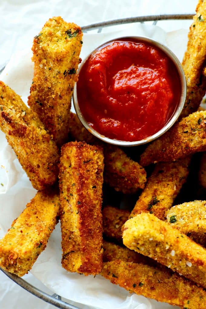 An overhead shot of air fryer eggplant fries in a basket with a bowl of marinara.